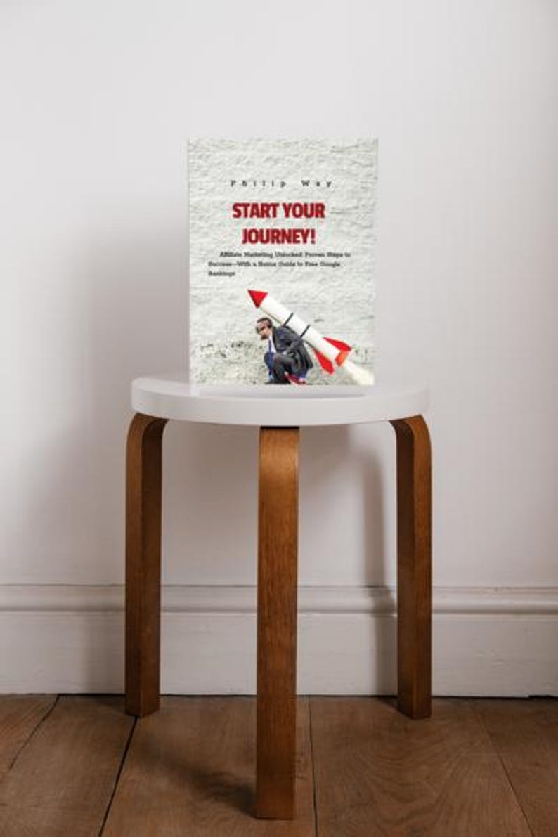 May include: A book titled "Start Your Journey!" with a rocket illustration, resting on a small, round, white table with wooden legs. The book cover features text and an image of a person with a rocket.