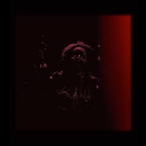 Puede incluir: Imagen oscura y siniestra de una mu&ntilde;eca con ojos brillantes, sobre un fondo negro con una franja vertical roja. La mu&ntilde;eca tiene el pelo desordenado y una expresi&oacute;n siniestra, creando una atm&oacute;sfera espeluznante.