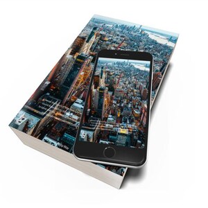 Op de afbeelding: Een hardcover boek en een smartphone met een stadsbeeld. Het boek heeft een stadsbeeld op de cover en de telefoon toont een vergelijkbaar luchtfoto. Het boek en de telefoon staan op een witte achtergrond.