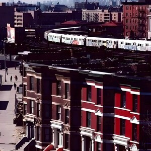 May include: Cityscape featuring a subway train curving through a neighborhood with brick buildings. The buildings are a mix of red and brown, with white trim. The distant skyline includes skyscrapers. The image has a vintage, slightly faded aesthetic.