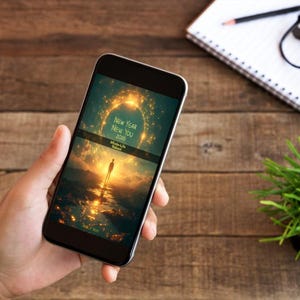 Może przedstawiać: Smartfon wyświetla motywacyjny obraz z tekstem "New Year New You 2026 Whole-Life Reboot". Telefon trzymany jest w dłoni, na tle drewnianego biurka, notatnika, okular&oacute;w, oł&oacute;wka i małej rośliny.