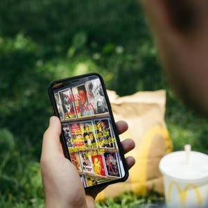 K&ouml;nnte beinhalten: Eine Person h&auml;lt ein Smartphone mit Buchcovern mit dem Text "MUSIC'S LEGACY" und "Rock and Roll from the Roaring Twenties to the Digital Age." Ein McDonald's-Becher und eine T&uuml;te sind im Hintergrund.