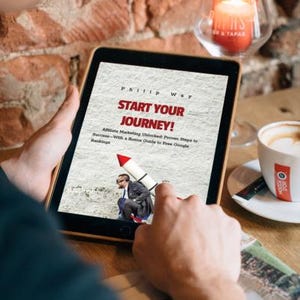 May include: A person holding a tablet displaying the book cover "Start Your Journey!" by Phillip Way. The cover features a man on a rocket. A lit candle and a cup of coffee are in the background.