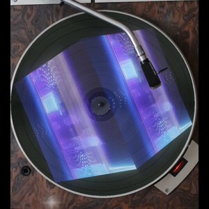May include: A vintage record player with a black turntable and a silver tone arm. A record is playing on the turntable, and the record is illuminated with a blue and purple light.