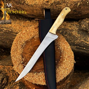 May include: A hunting knife with a light-colored wooden handle and a long, curved stainless steel blade. The knife is in a black leather sheath with red stitching. The text "AR HUNTING" is visible in the upper left corner.