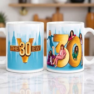 Puede incluir: Dos tazas de cerámica blanca con la marca del 30 aniversario de The View. Una taza muestra el logotipo dorado 30 sobre un horizonte azul. La otra taza muestra el mismo logotipo con siete personas posando alrededor de los grandes números dorados.