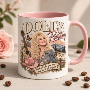 Op de afbeelding: Een witte keramische mok met een roze binnenkant en handvat, voorzien van een afbeelding van Dolly Parton, een gitaar, een roze cowboyhoed, vlinders en bloemen. De tekst luidt DOLLY Parton, 1946-2025 en Find out who you are and do it on purpose.