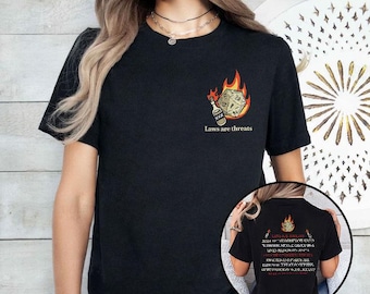 May include: Black t-shirt featuring a graphic of a flaming die and a bottle, with the text "Laws are threats." The design includes a 20-sided die. The back of the shirt has additional text and a similar graphic.