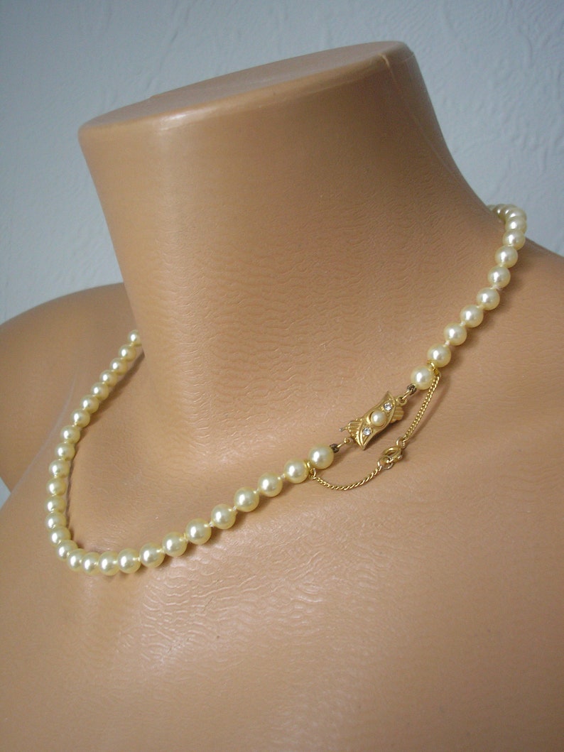 May include: A classic pearl necklace with a gold clasp. The necklace is made of white pearls and has a simple design.