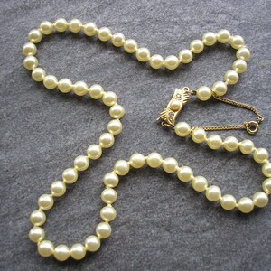 May include: A strand of cream-colored faux pearl beads with a gold clasp featuring a small clear rhinestone.