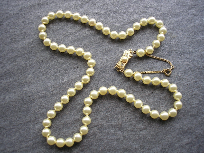 May include: A strand of cream-colored faux pearl beads with a gold clasp featuring a small clear rhinestone.