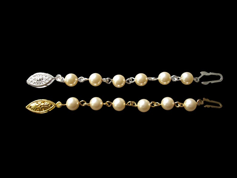May include: Two strands of faux pearl jewellery with gold and silver leaf-shaped clasps. Each strand has 8 pearls and a clasp.