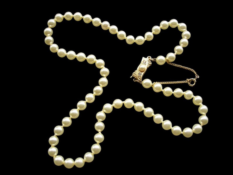May include: A classic pearl necklace with a gold clasp. The necklace is made of white pearls and has a simple design.