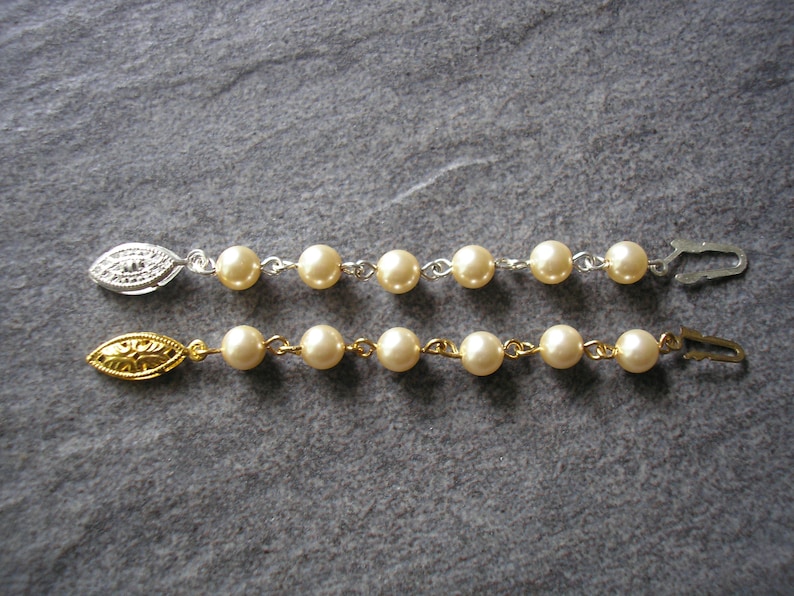 May include: Two pearl necklaces with gold and silver clasps. Each necklace has a series of white pearls connected by a thin metal chain.