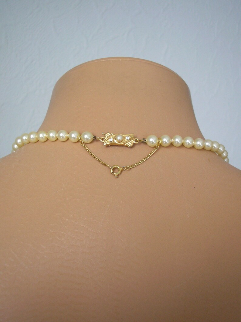 May include: A gold chain necklace with a gold clasp and a row of white pearls.