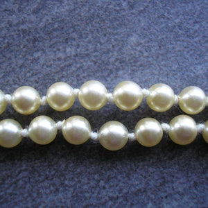 May include: A strand of cream-colored pearl beads strung on a white thread.
