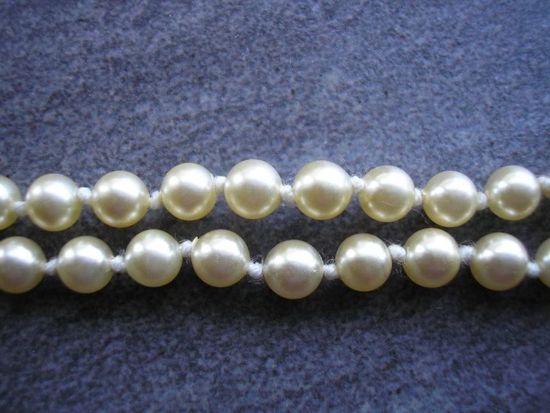 May include: A strand of cream-colored pearl beads strung on a white thread.