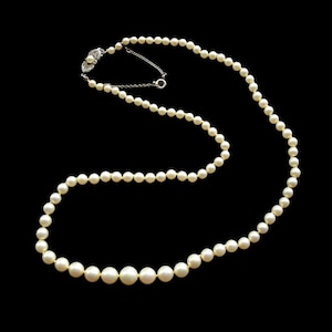 May include: A classic pearl necklace with a silver clasp. The necklace features graduated, creamy white pearls, ranging in size from small to large. The pearls are strung together, creating a timeless piece of jewelry.