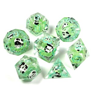 May include: Set of seven polyhedral dice with a panda bear theme. The dice are clear with a green core, and feature black and white panda illustrations and teal numbering. The dice are designed for tabletop role-playing games.