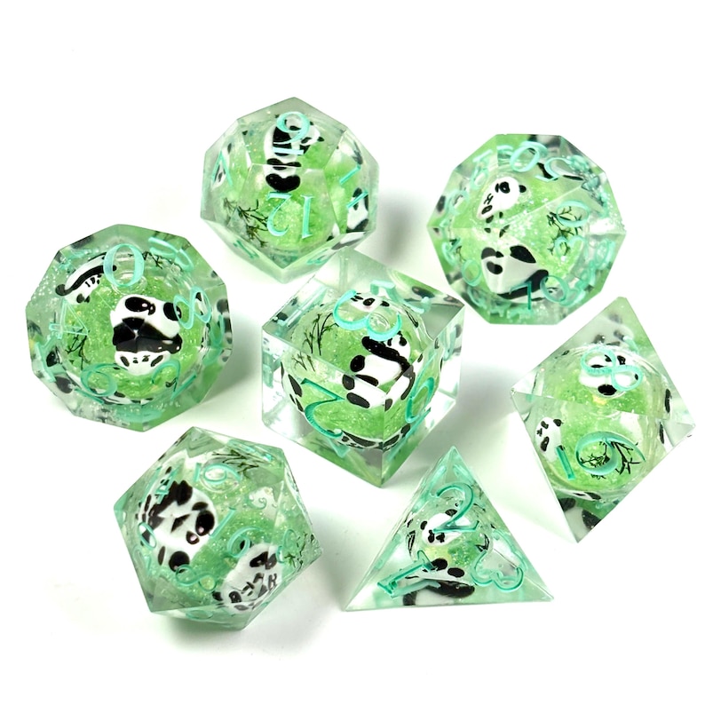 May include: Set of seven polyhedral dice with a panda bear theme. The dice are clear with a green core, and feature black and white panda illustrations and teal numbering. The dice are designed for tabletop role-playing games.