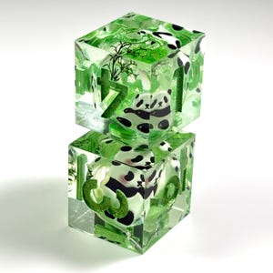 May include: Two stacked translucent green resin dice featuring embedded panda illustrations and green glitter numerals. The dice contain small black and white panda figures, green foliage elements, and clear resin material with a glossy finish.