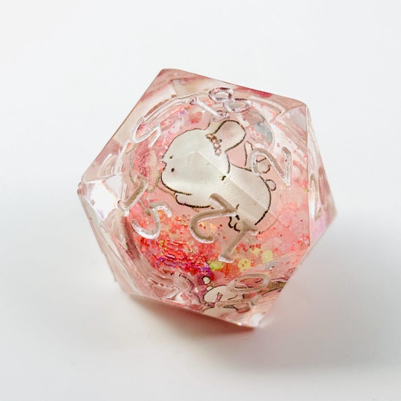 Peut inclure: Un d&eacute; clair &agrave; multiples faces avec un int&eacute;rieur rose et rouge paillet&eacute;. Un lapin de dessin anim&eacute; blanc est repr&eacute;sent&eacute; sur un c&ocirc;t&eacute;. Les chiffres sont argent&eacute;s. Ce d&eacute; unique est parfait pour les jeux de soci&eacute;t&eacute;.