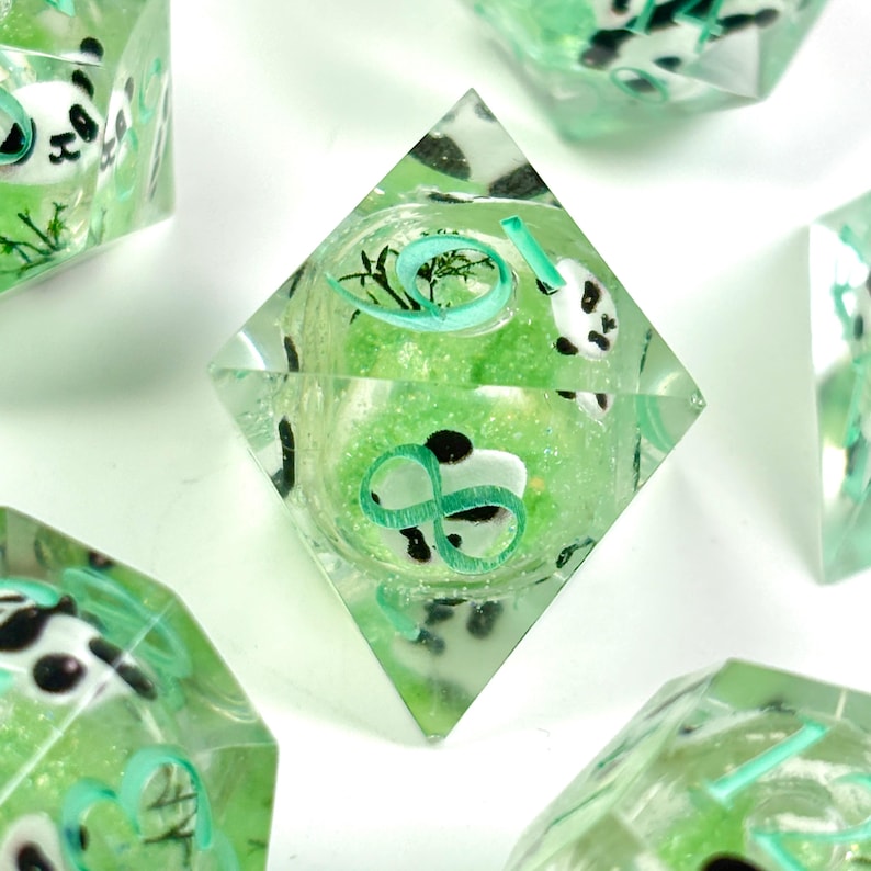May include: Clear, multi-sided dice with a panda bear design. The dice are filled with a light green glitter and feature panda faces, green swirls, and the number 10 in a light green color. The dice are set against a white background.