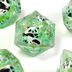 May include: A set of polyhedral dice with a panda bear theme. The dice are clear with a green tint, and the panda is black and white. The numbers are in a light green color. The dice are designed for tabletop games.