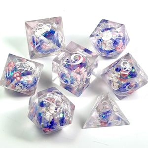 Peut inclure: Ensemble de sept d&eacute;s en r&eacute;sine transparente avec des motifs floraux et de lapins. Les d&eacute;s pr&eacute;sentent des accents bleus, roses et blancs, avec des chiffres blancs. Les d&eacute;s sont de formes g&eacute;om&eacute;triques vari&eacute;es, dont un cube, un d20 et un d4.