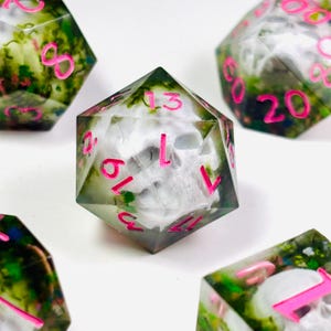 Op de afbeelding: Set polyhedrale dobbelstenen met een schedelontwerp. De dobbelstenen zijn helder met een groen en wit interieur, en de cijfers zijn felroze. De dobbelstenen zijn voor tabletopspellen.