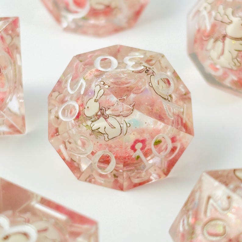 Peut inclure: Un ensemble de d&eacute;s poly&eacute;driques avec un motif floral rose et des illustrations de lapins blancs. Les d&eacute;s sont transparents avec des chiffres blancs et conviennent aux jeux de soci&eacute;t&eacute;. Les d&eacute;s sont en r&eacute;sine.