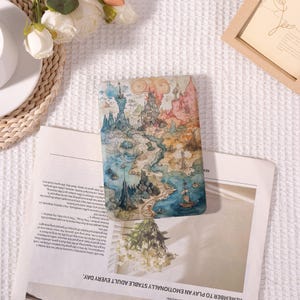 May include: A colorful fantasy map design on a rectangular phone case. The case features a detailed illustration of a fantastical landscape with castles, mountains, and a sailing ship. The case is resting on a newspaper.