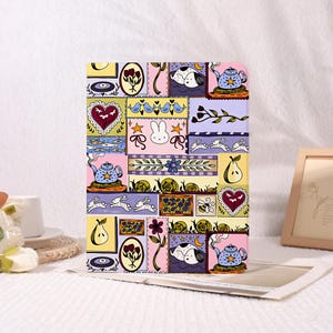 May include: A colorful tablet case with a patchwork design featuring whimsical illustrations. The design includes rabbits, teapots, hearts, pears, and snails in a variety of colors including pink, yellow, blue, and purple. The case is rectangular.