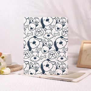 May include: A white tablet case featuring a repeating pattern of cartoon dog faces and bones in navy blue. The case is rectangular and appears to be made of a smooth material. The design is playful and suitable for pet lovers.