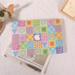 May include: A laptop hard shell case featuring a colorful patchwork grid design. The pattern consists of squares with various motifs including hearts, flowers, plaid, and polka dots in shades of pink, blue, yellow, green, and orange.