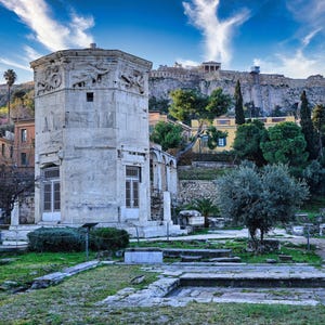 Peut inclure: Une tour de pierre blanche avec une base carrée et un toit plat. La tour est entourée d'herbe verte et d'arbres. Au fond, on peut voir une colline avec des bâtiments et une grande formation rocheuse.