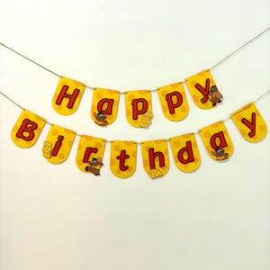 May include: A yellow and red Happy Birthday banner with a cartoon mouse character and cheese designs. The banner is strung together with twine.