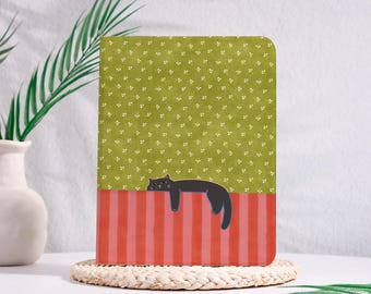 May include: A rectangular notebook featuring a green cover with a small white floral pattern on the top half and vertical red and pink stripes on the bottom half. A black cat is illustrated lying across the border between the two patterns.