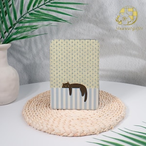 May include: A rectangular decorative box with a floral pattern and a sleeping cat illustration. The box has a light blue and white striped bottom section. The box is resting on a woven mat.