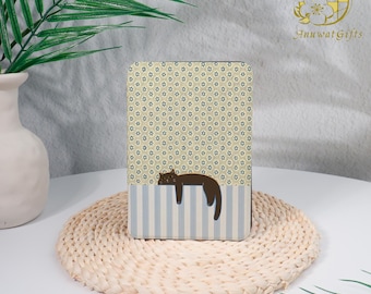 May include: A rectangular decorative box with a floral pattern and a sleeping cat illustration. The box has a light blue and white striped bottom section. The box is resting on a woven mat.