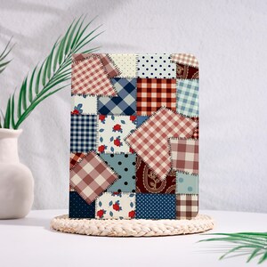 Op de afbeelding: Een rechthoekig notitieboek met een patchwork-ontwerp. De kaft heeft vierkanten met verschillende patronen, waaronder ruitjes, stippen en bloemenprints, in tinten rood, blauw en beige. Het notitieboek wordt weergegeven op een ronde, geweven onderzetter.