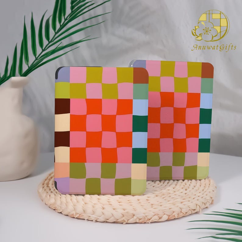 Pode incluir: Duas bases quadradas com um padr&atilde;o xadrez colorido em tons de laranja, rosa, verde e azul. As bases s&atilde;o exibidas em uma esteira tecida, com um vaso branco e vegeta&ccedil;&atilde;o ao fundo.