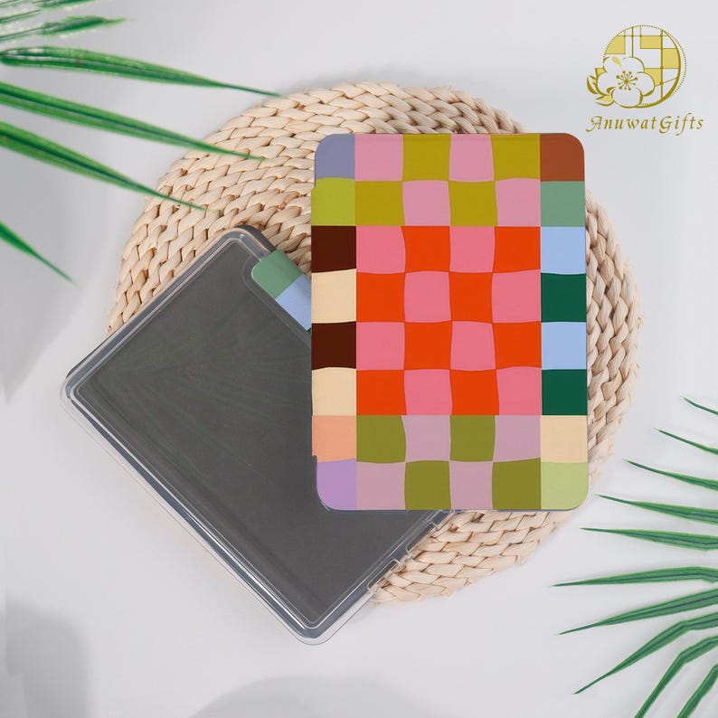 Pode incluir: Uma garrafa de &aacute;gua retangular transparente com uma capa estampada com padr&otilde;es coloridos em tons de rosa, laranja, verde e roxo. A garrafa &eacute; parcialmente vis&iacute;vel, repousando sobre uma esteira tecida com folhas verdes ao fundo.