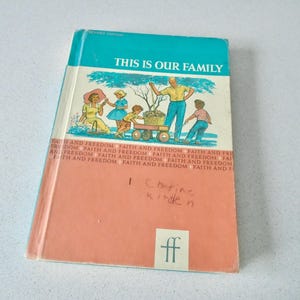 May include: A vintage book titled "THIS IS OUR FAMILY" with a teal and peach cover. The cover features a family illustration and the words "FAITH AND FREEDOM" along the edges. Handwritten text is visible on the peach cover.