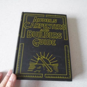 May include: A black book with gold lettering titled "Audels Carpenters and Builders Guide". The cover features a stylized illustration of a sunrise and a carpenter's tool.