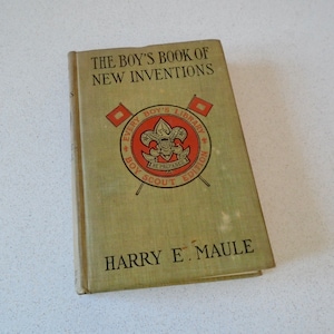 May include: A green book titled "The Boy's Book of New Inventions" with a Boy Scout emblem on the cover. The book is part of the "Every Boy's Library" series.