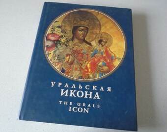 May include: A hardcover book with a dark blue cover featuring a religious icon in a circular frame. The icon depicts a woman and child with halos, surrounded by gold and floral elements. The title "УРАЛЬСКАЯ ИКОНА THE URALS ICON" is printed in white.