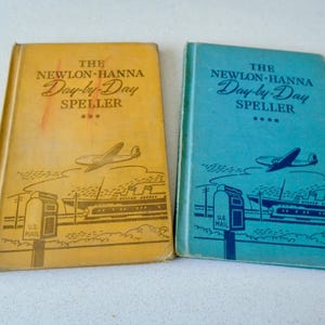 May include: Two vintage "The Newlon-Hanna Day-by-Day Speller" books. One is yellow, the other is blue. Each book features an illustration of a plane, a ship, and a US Mail post. The text on the cover reads "The Newlon-Hanna Day-by-Day Speller".