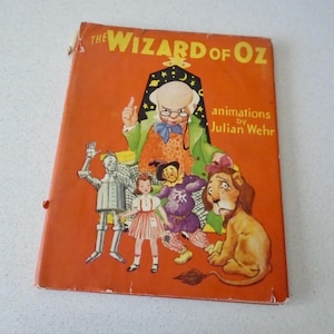 May include: A vintage hardcover book titled The Wizard of Oz with animations by Julian Wehr. The orange cover features illustrations of the Tin Man, Dorothy, the Scarecrow, the Cowardly Lion, and the Wizard against a dark arched doorway.