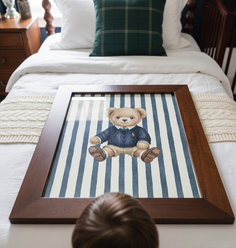 May include: A framed print featuring a watercolor illustration of a teddy bear wearing a blue sweater and khaki shorts, set against a backdrop of blue and white vertical stripes. The frame is a dark brown wood.